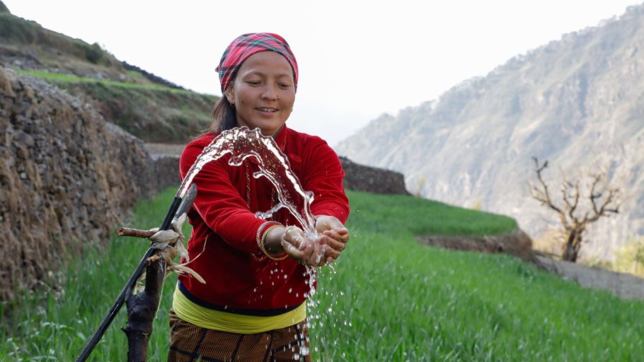 A woman holding her hands out to catch a spurt of water from a hose.