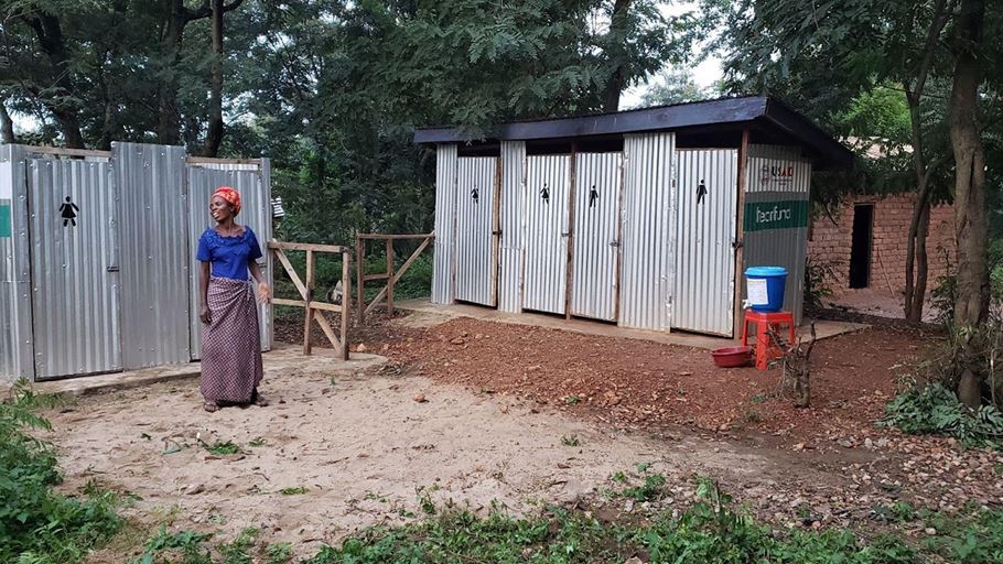 A woman standing outside some outdoor toilet cubicles