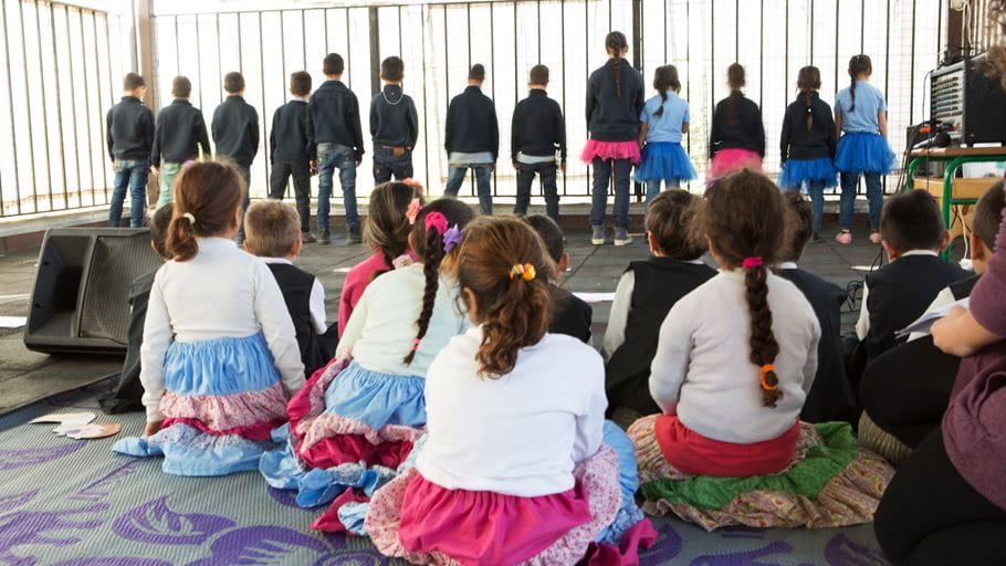 A group of children sitting down watching another group of children putting on a performance