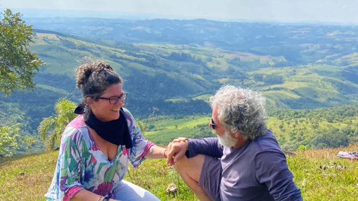 A woman and a man sitting on a hill with rolling green hills in the background