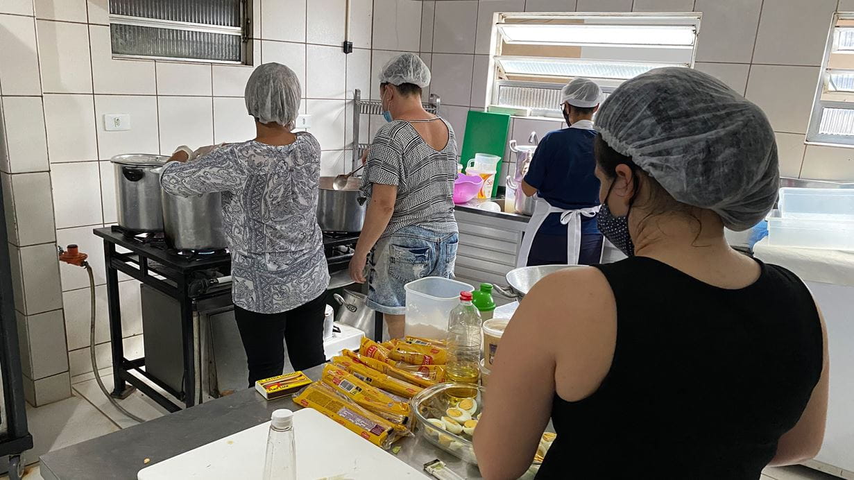 Four people preparing food in a kitchen with hair nets on