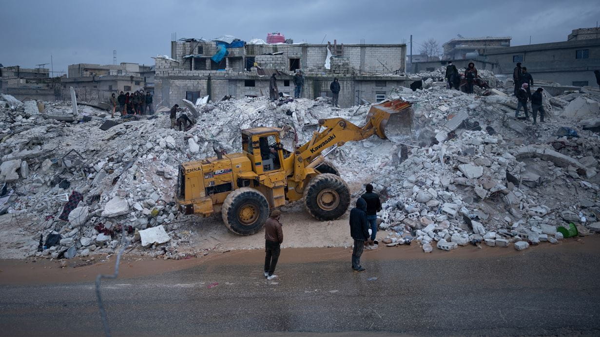A heavy vehicles trying to remove rubble from a destroyed building.