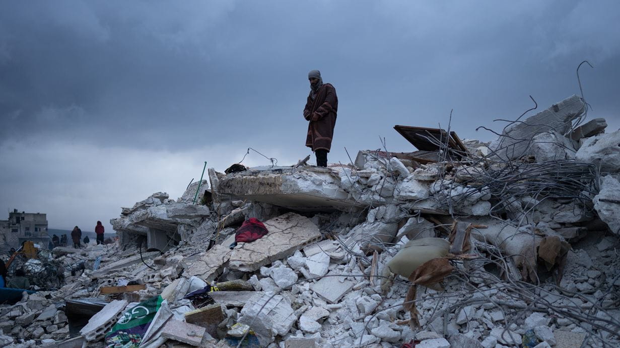 A man standing on the rubble of a destroyed building.