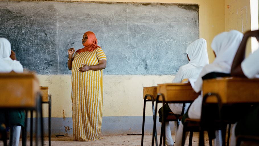 A teacher stood by a blackboard in front of a class of children.