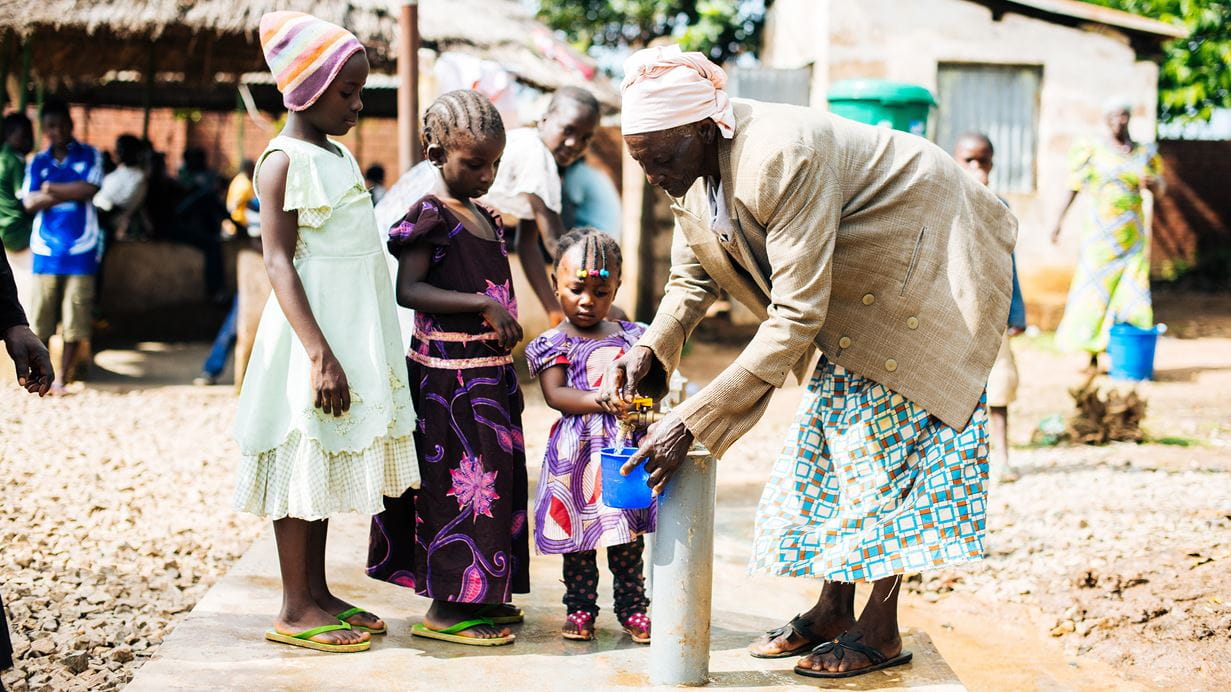 A woman and three children stand around a water pump
