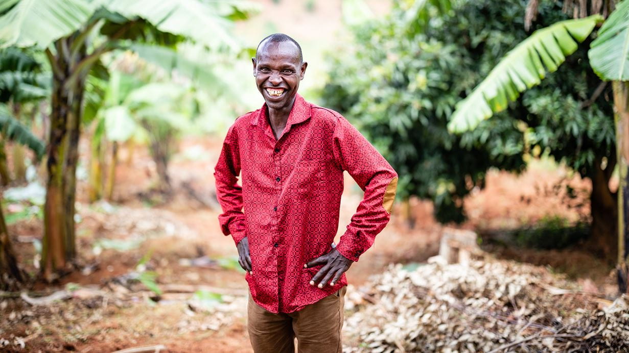 A smiling man in a red shirt with trees in the backgroundA smiling man in a red shirt with trees in the background