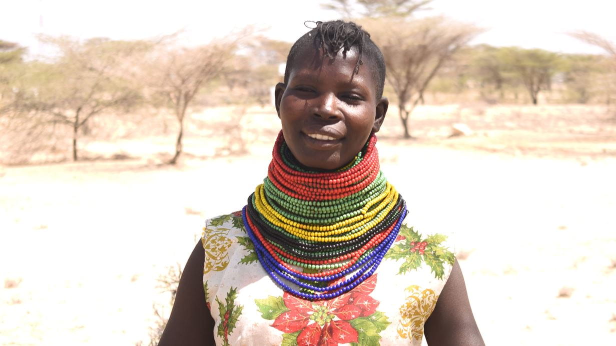 A smiling woman wearing a large amount of colourful necklaces