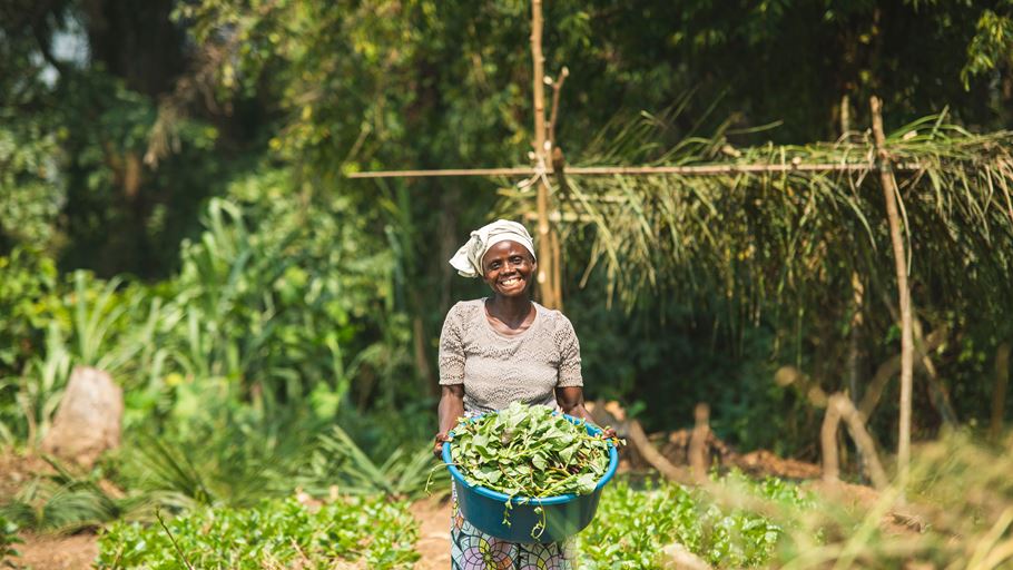 A smiling woman in grey holding up a container of crops