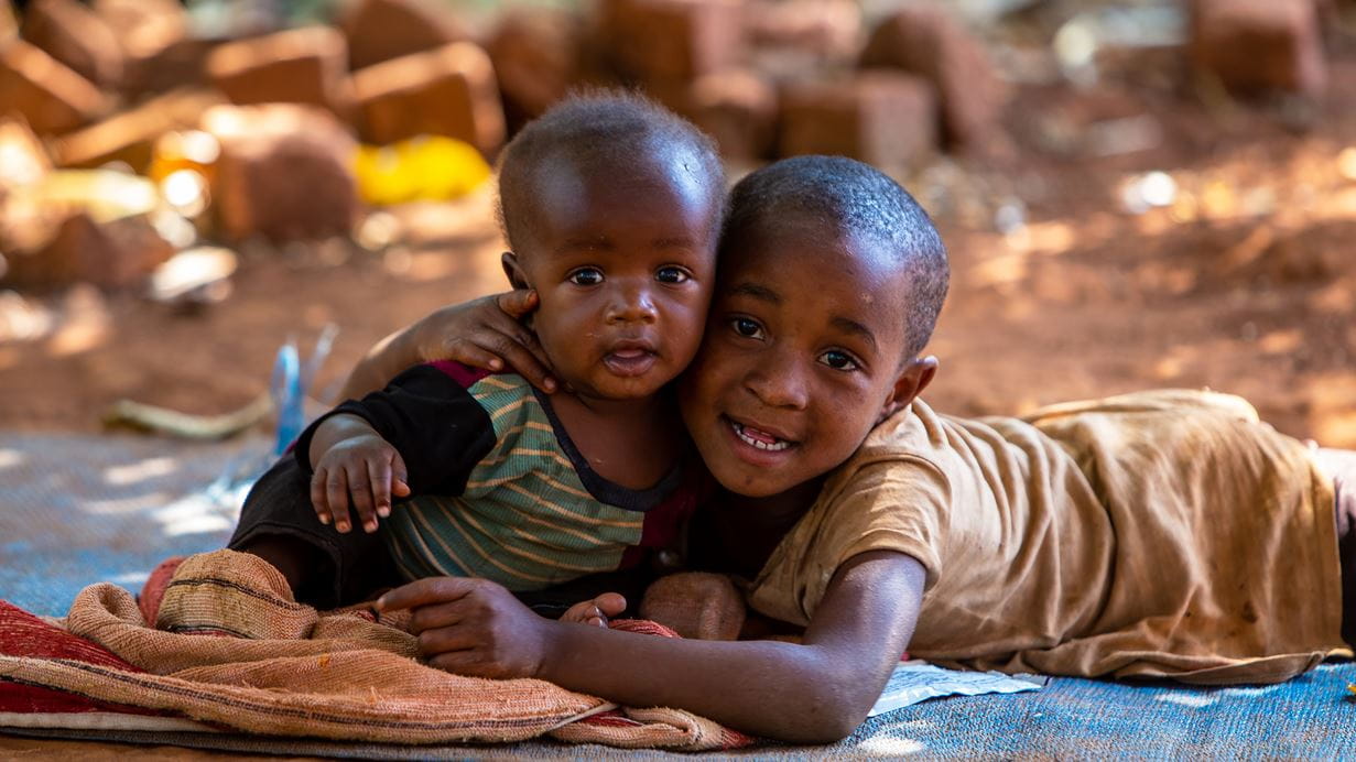 A small African boy smiles as he hugs his baby brother.