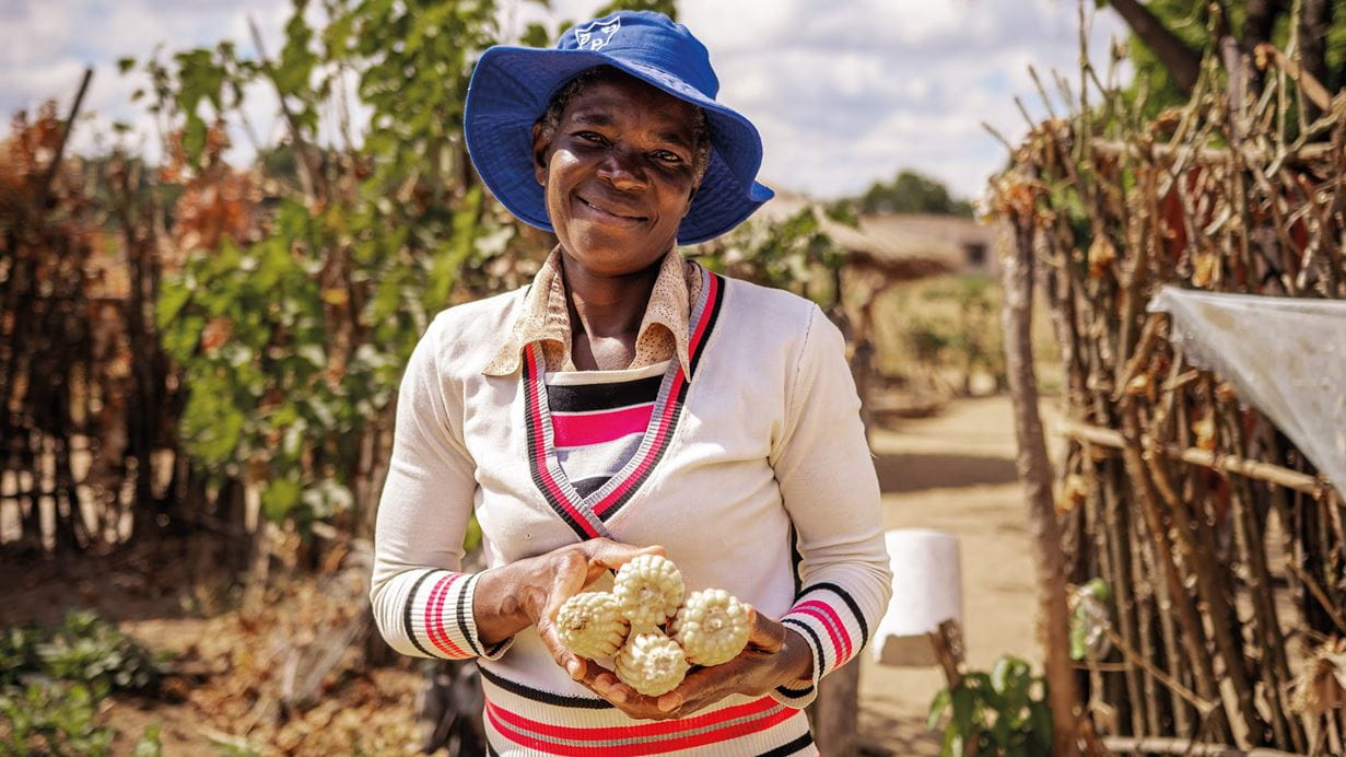 A woman smiles as she holds the corn she’s grown.