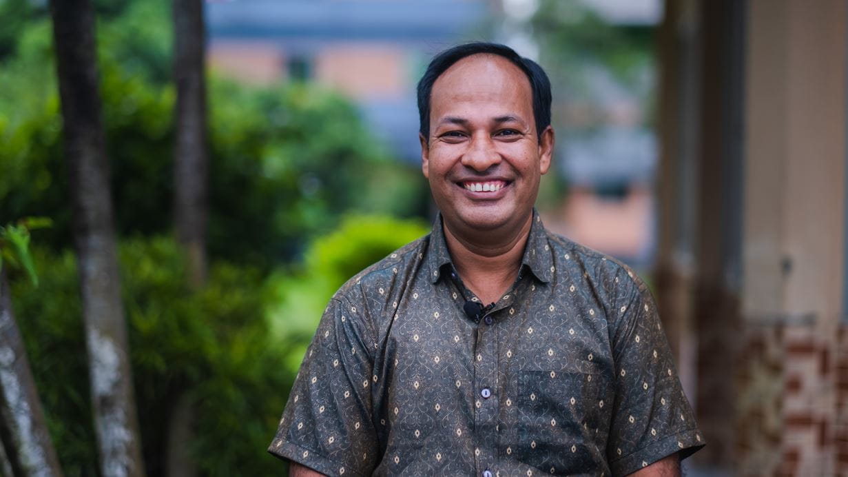 Pastor Asit wears a blue shirt and smiles broadly for the camera.