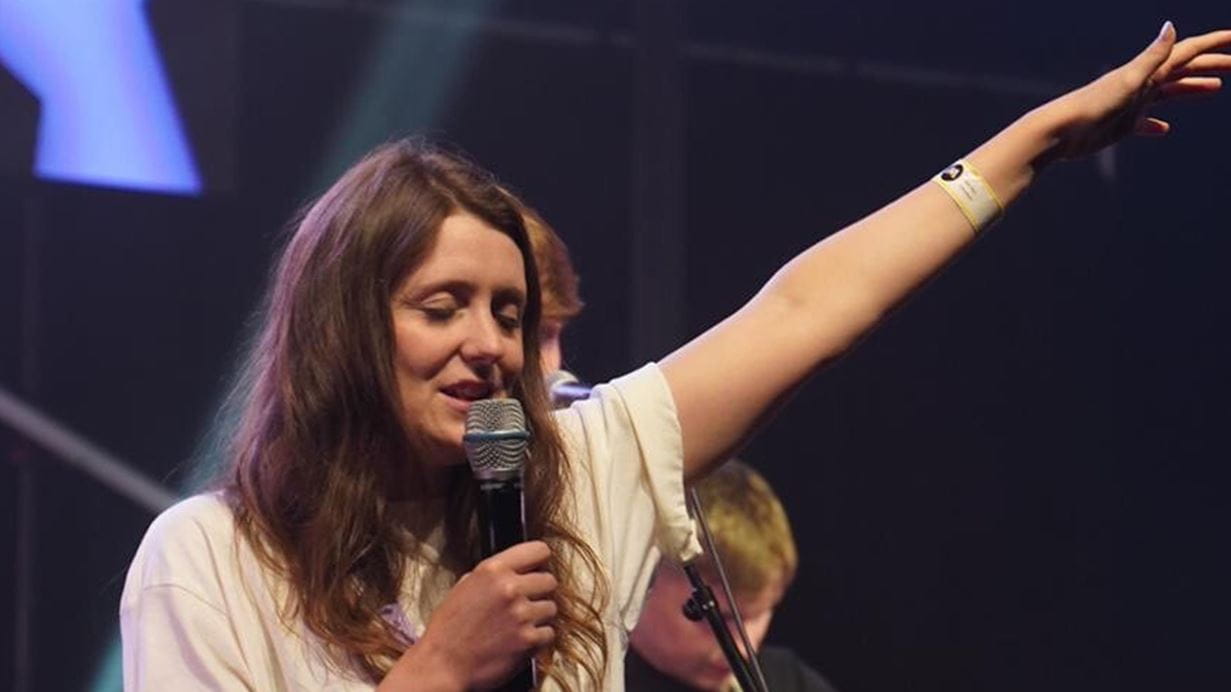 A close up of Bee Roy on stage with her eyes closed, holding a mic and her other hand in the air.