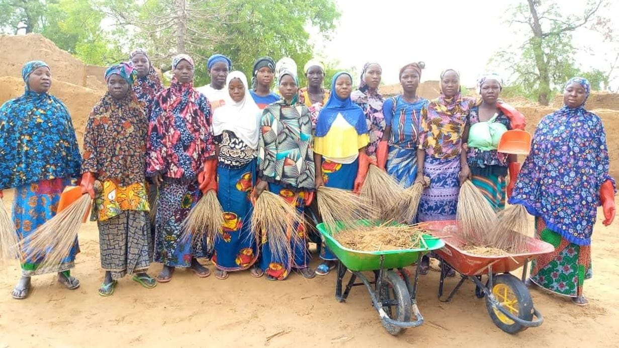 Mariam and her group of awareness-raising women stand together in the sunshine for a photograph with the wheelbarrows they use to clean up their community.