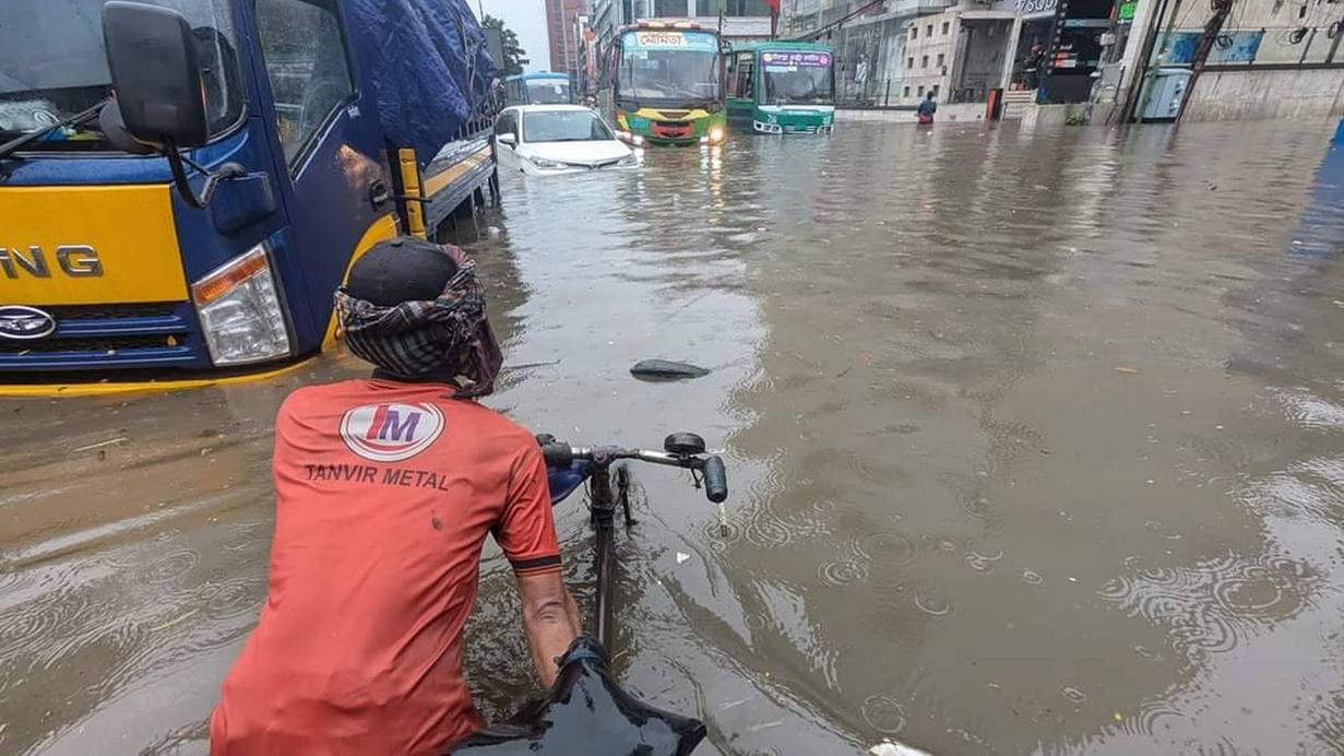 A bicycle and buses try to make their way through roads flooded by monsoon rains in Dhaka 