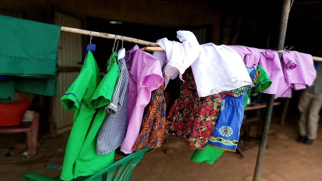 Brightly coloured items of clothing and school uniform that Jenifer has sewn hang in a row on a rail, ready to be sold.
