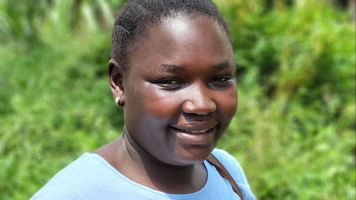 Claudine, a woman in a light blue shirt, smiles at the camera