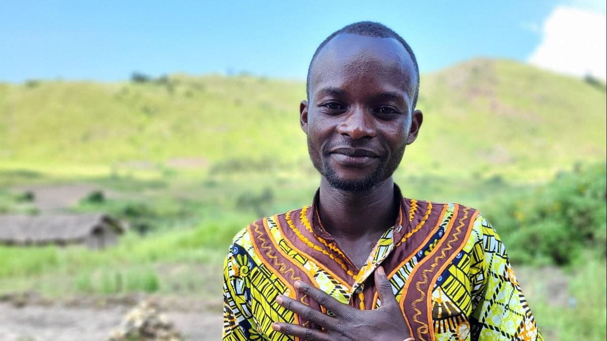 Jefte, wearing a traditionally patterned shirt, smiles at the camera