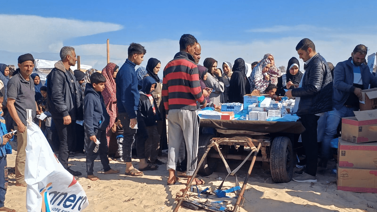 A large number of men and women of all ages queue outside a mobile clinic to receive medicines or medical treatment in Gaza.
