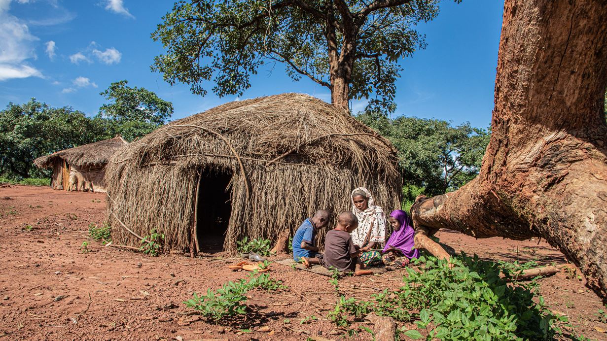 Adama sits together with her three grandchildren in the sunshine outside the house they built of straw and wood after they were forced to flee their home because of conflict.