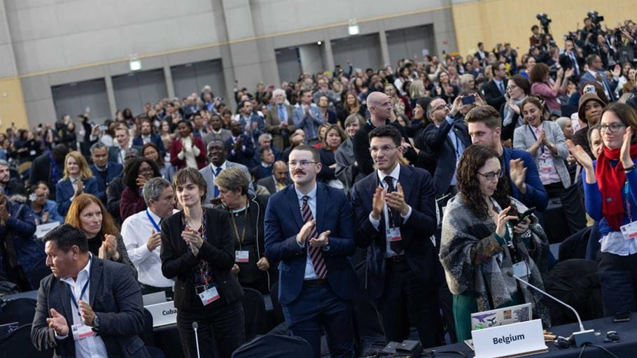 Hundreds of people of different nationalities stand to applaud a call to ‘stand up for ambition’.