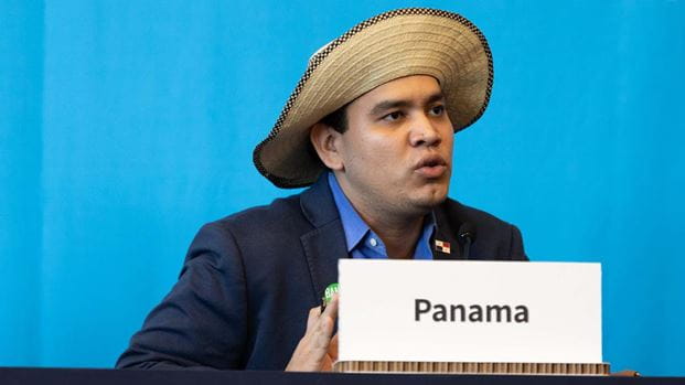 A man wearing a Panama hat speaks into a microphone.