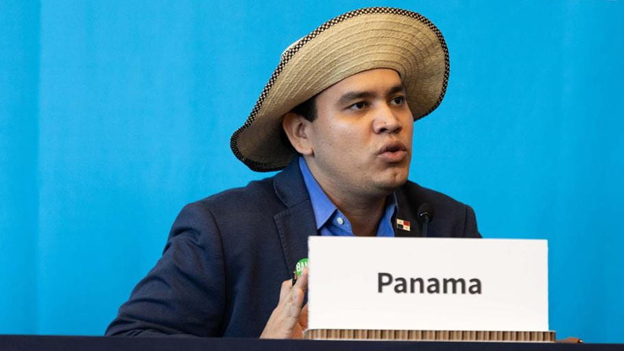 A man wearing a Panama hat speaks into a microphone.