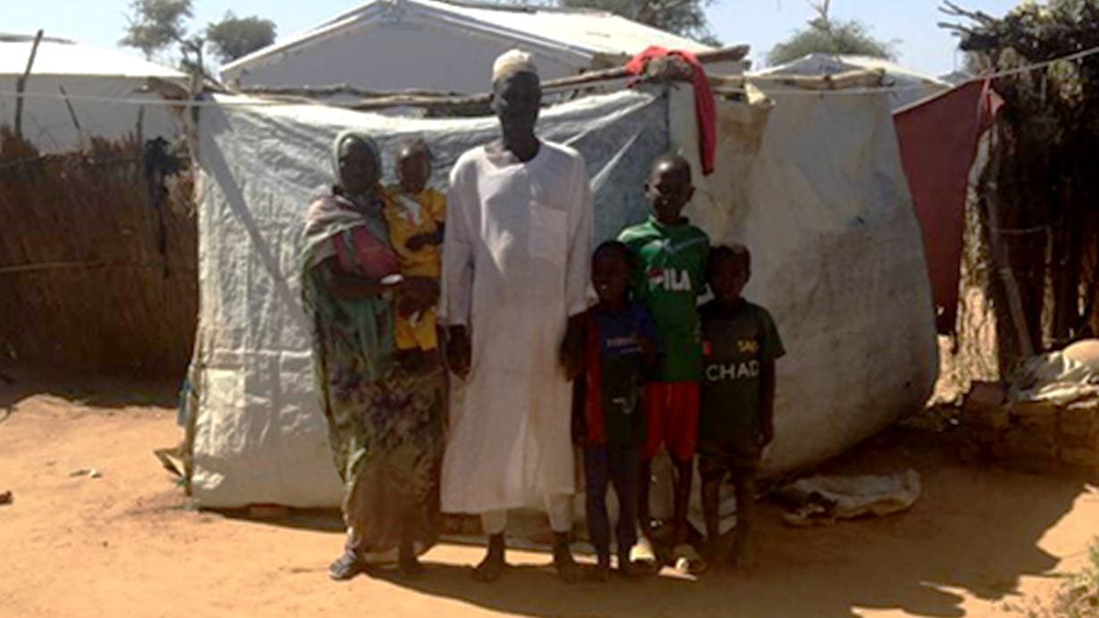 A family stand in front of a temporary shelter.