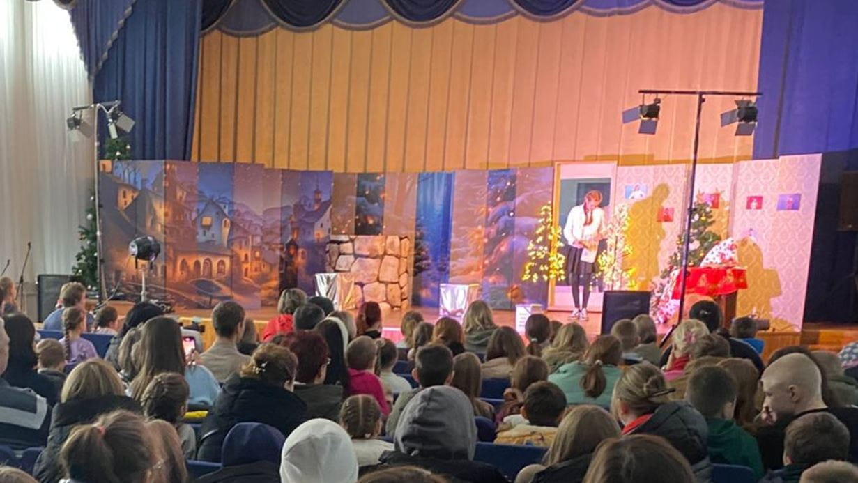 An audience watches a young woman perform on stage in front of a brightly-decorated set as part of a Christmas drama.