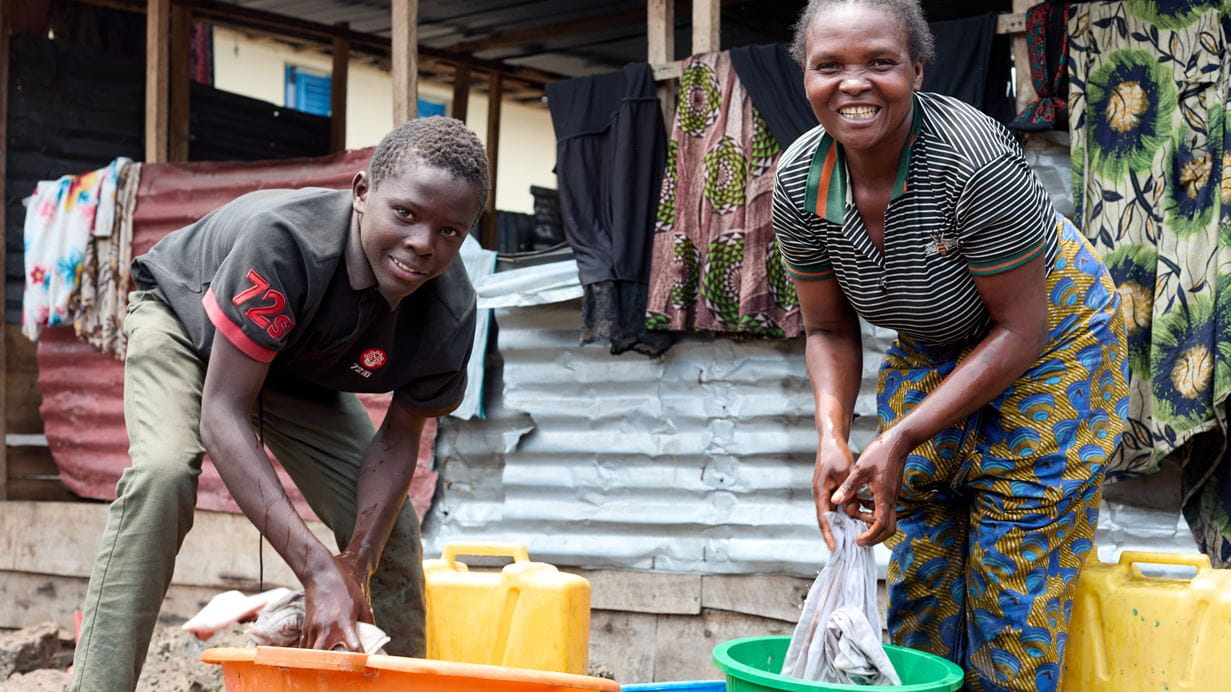 Rose and her son smile as they wash some clothes outside the classroom