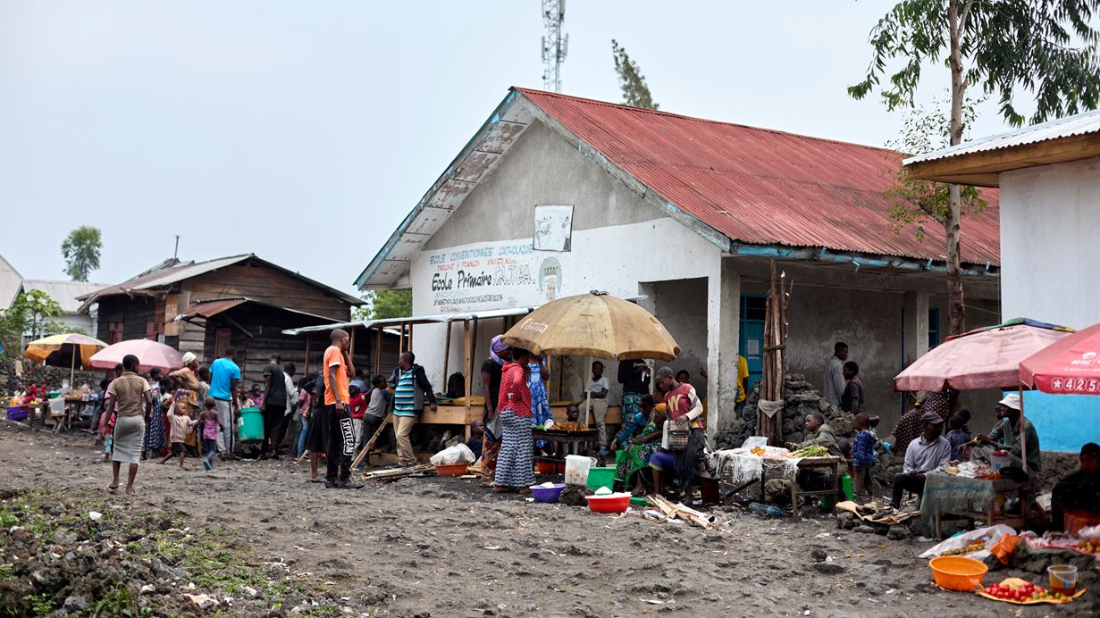 People sit under umbrellas to shade them from the sun outside a school being used as a shelter for IDPs in DRC