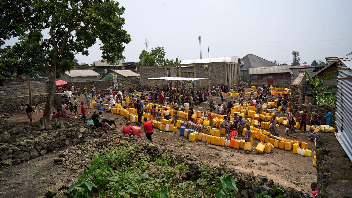 A long queue of yellow containers for carrying water zig zags across the ground while people wait with them to collect fresh water