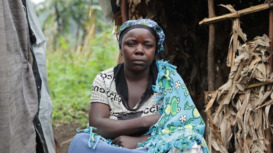 A woman sits facing the camera in front of a makeshift shelter