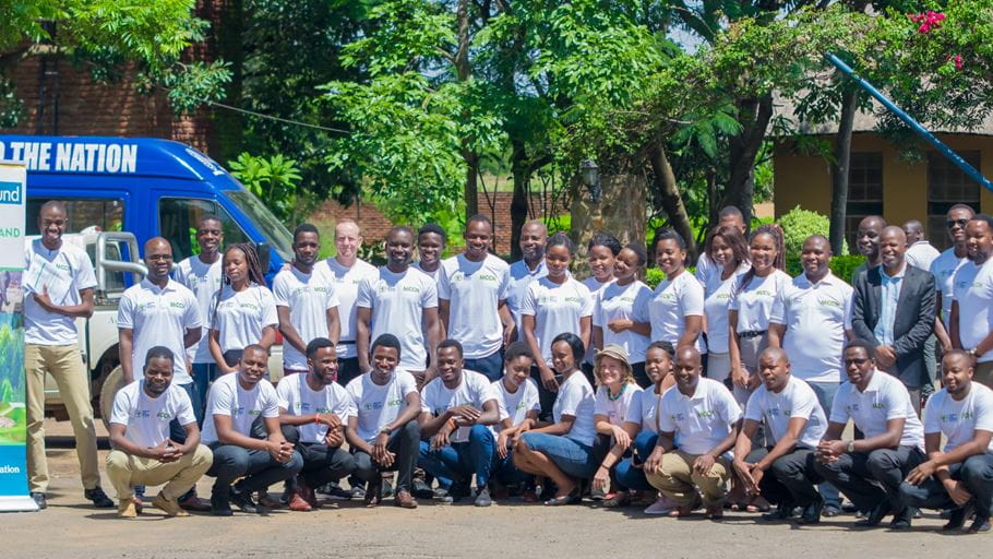 A group of people wearing MCCP T-shirts stand together outside under a blue sky