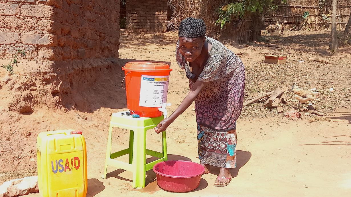 Woman washes hands at a simple water station in a rural area.