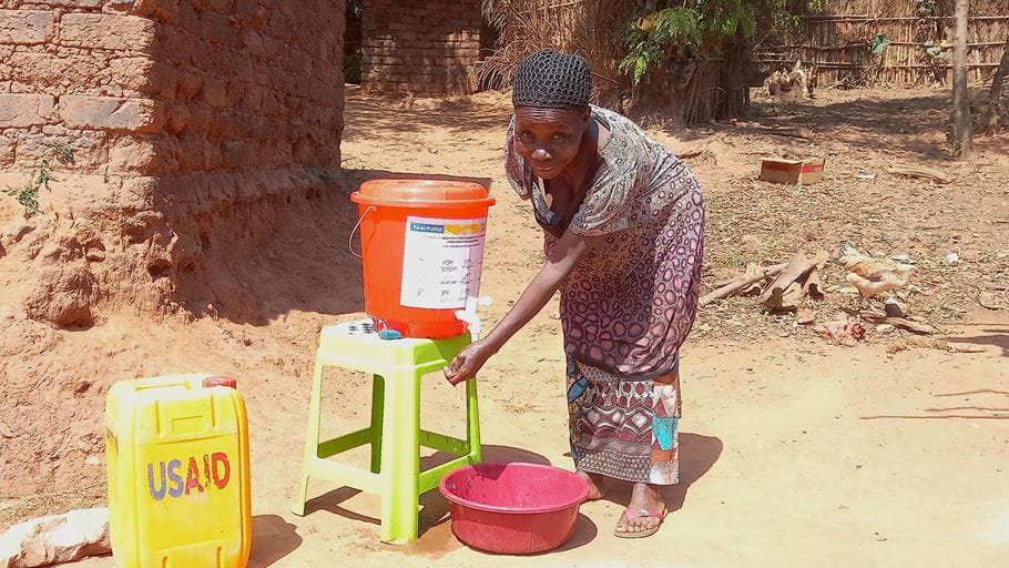 Woman washes hands at a simple water station in a rural area.