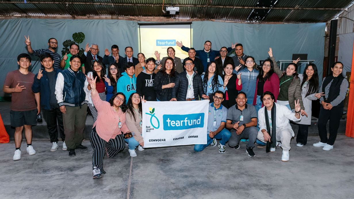 Group photo of Tearfund volunteers holding a banner, smiling and posing in an indoor setting.