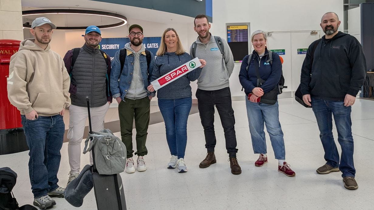 Group of seven people holding a SPAR banner in an airport terminal, smiling at the camera.