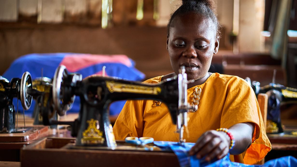 Woman in orange shirt sewing with vintage machine. Other sewing machines in background.
