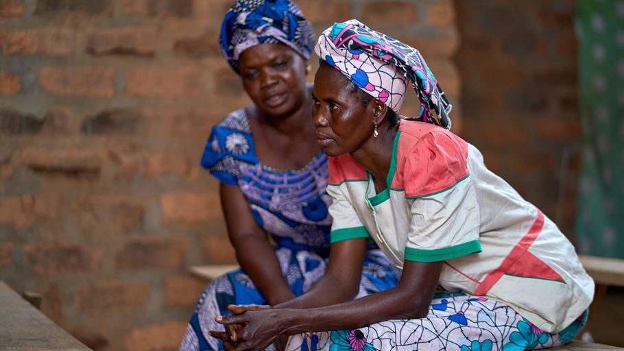 Two African women in colorful patterned clothing and headwraps sitting together.