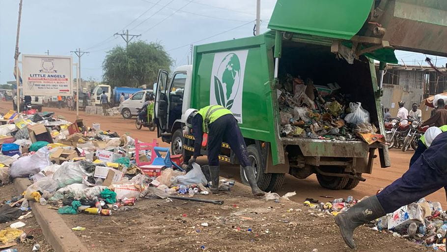 A street in Juba, South Sudan, where two EcoClean employees are gathering loose waste strewn across the ground and loading it into their green truck.