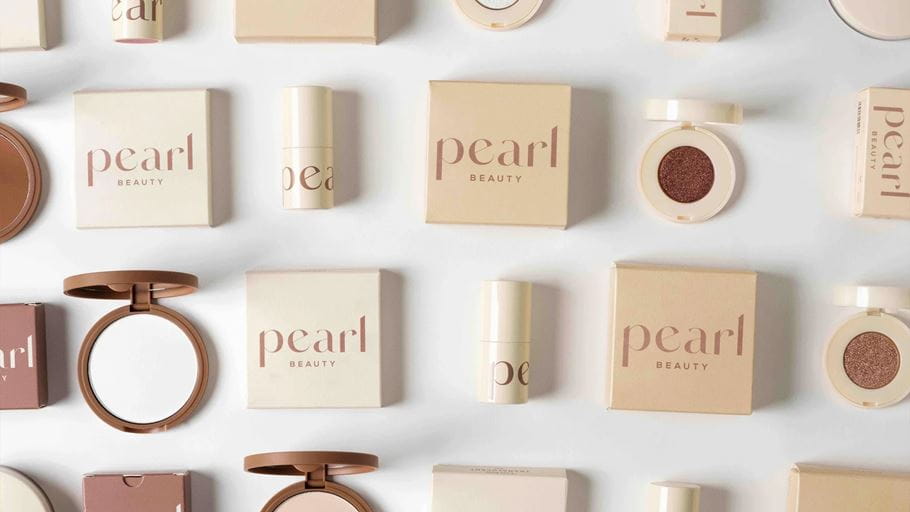 Overhead shot of Pearl Beauty makeup products in beige packaging, arranged on a white background.