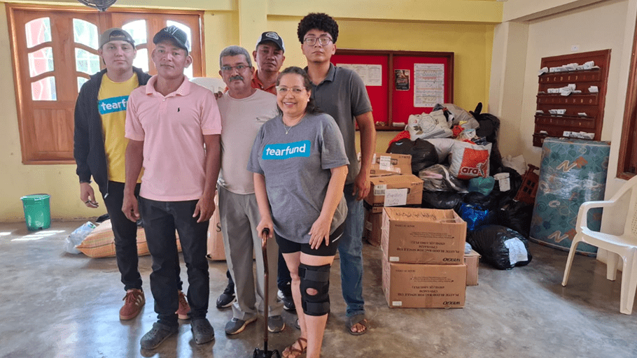 Six people stand together inside a room next to piles of donated bags and boxes, with Tearfund logos visible on some shirts.