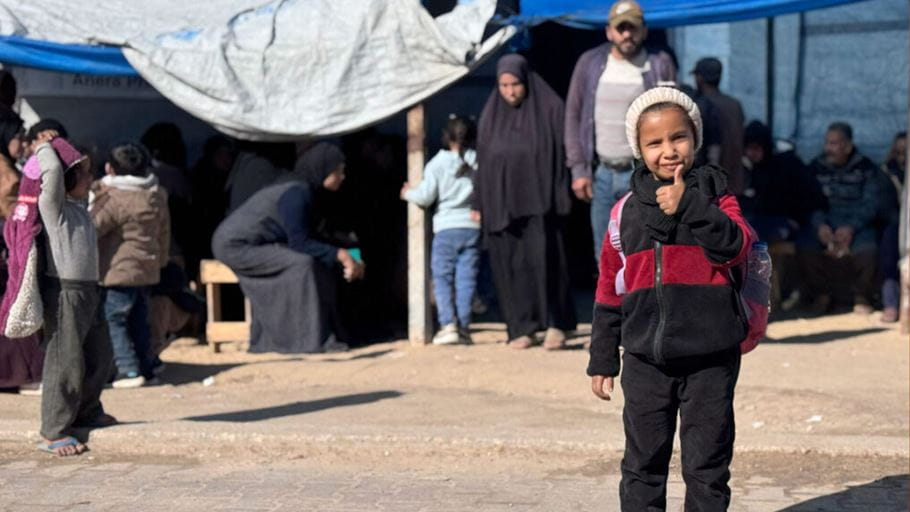 Young girl gives a thumbs up in front of a crowd outside a clinic.