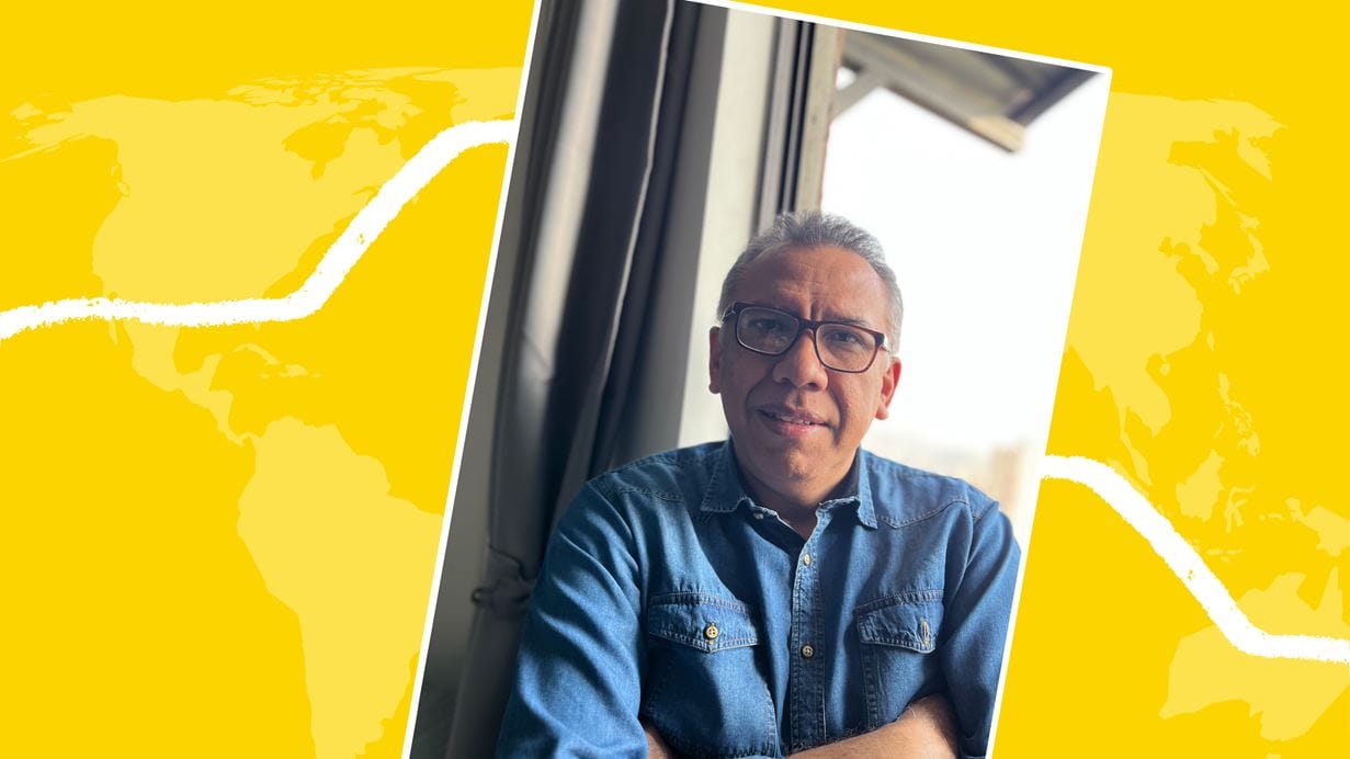 Man in denim shirt with arms crossed, smiling; yellow background with world map graphic.
