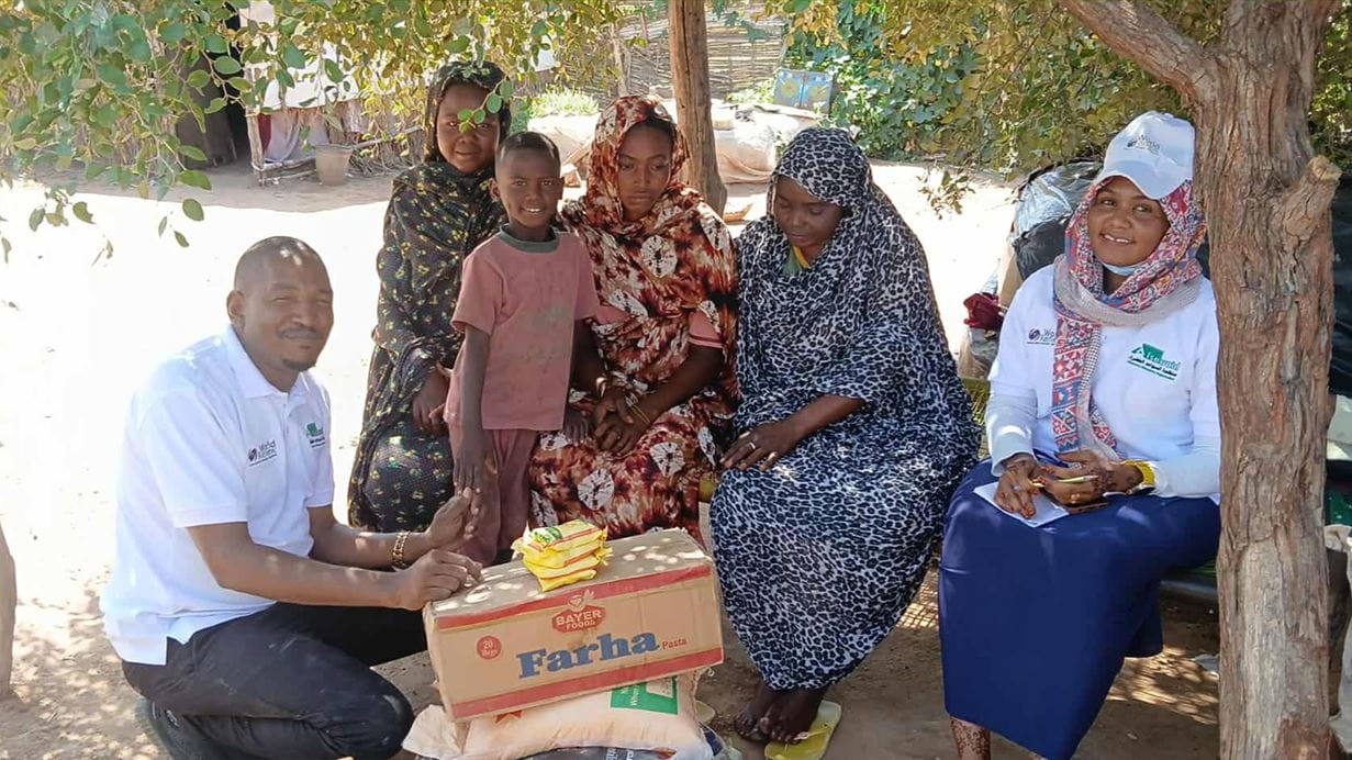 Group of women and a boy receive a food donation outdoors.