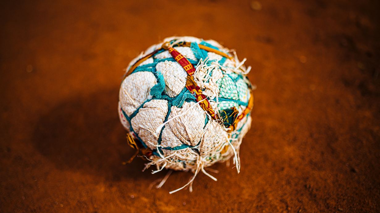 Worn, handmade patchwork fabric ball on a dusty reddish-brown ground.