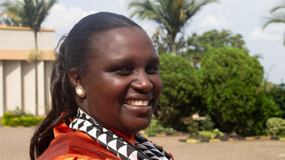A woman smiles at a camera side on, with trees in the background.