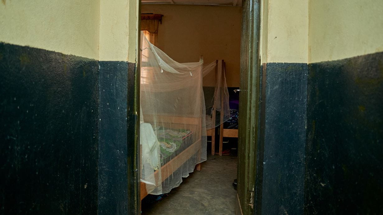 View through a doorway into a simple healthcare centre with a wooden bed covered by a mosquito net.