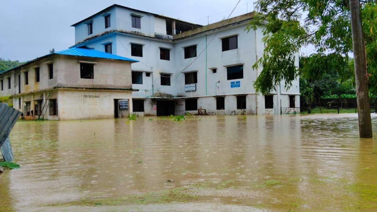 Two buildings partially submerged in muddy floodwaters under a grey sky.