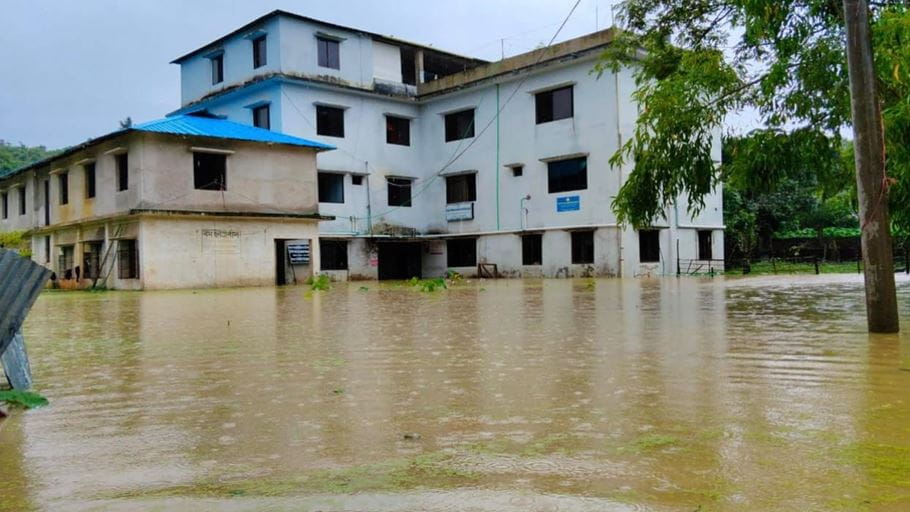 Two buildings partially submerged in muddy floodwaters under a grey sky.
